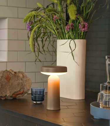 Candeeiro de mesa portátil Muuto sobre bancada de cozinha escura com decoração floral.