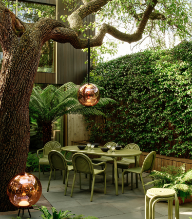 Candeeiros de exterior Tom Dixon num elegante jardim com área de refeições sob uma árvore antiga.