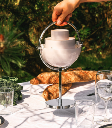 Candeeiro de mesa portátil GUBI sobre mesa de jardim elegantemente posta à luz do sol.
