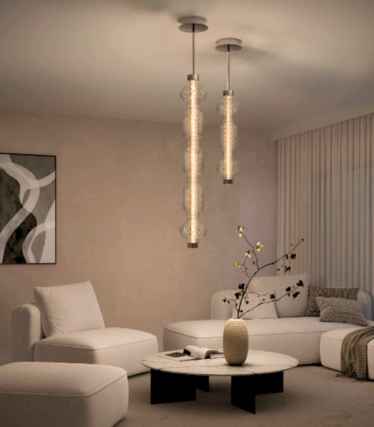 Dois elegantes candeeiros suspensos de vidro sobre uma mesa de centro em mármore, numa sala luminosa com sofá branco e poltrona.