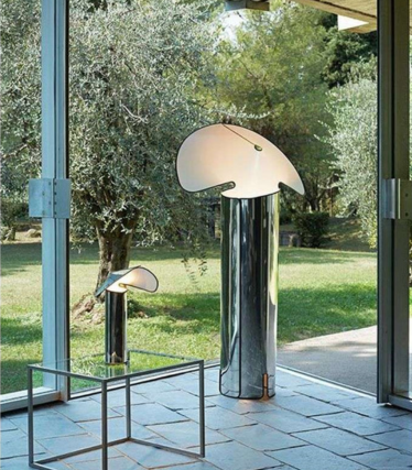 Dois candeeiros de pé brilhantes com abajures curvos em forma de folha diante de uma janela com vista para o jardim.